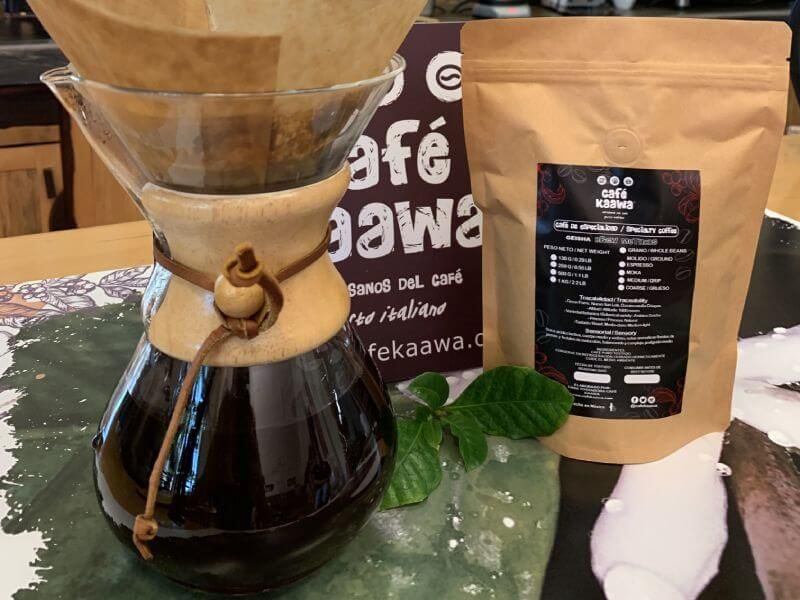 Coffee brewing in a pour over glass coffee pot besides a bag of specialty coffee geisha