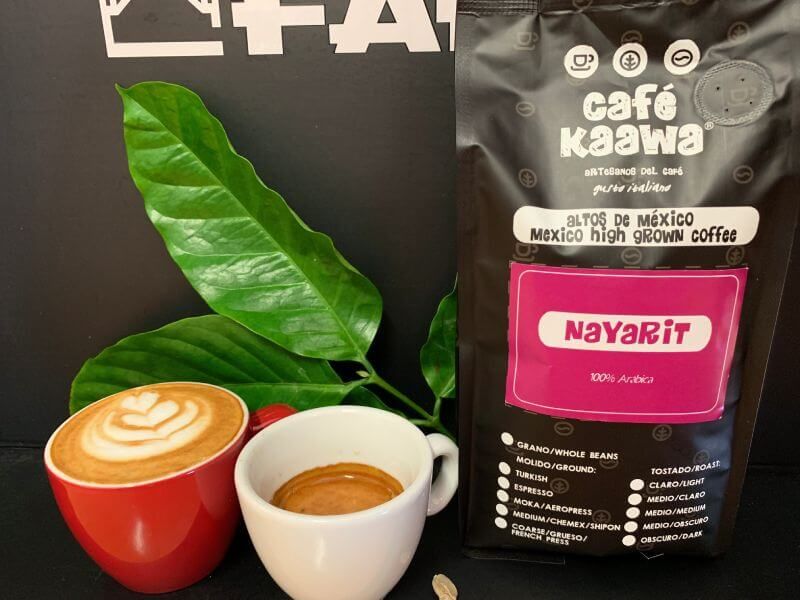 Green leafs on the background and a bag of Café Kaawa Nayarit, in front there's an espresso and a cappuccino with a tulip design